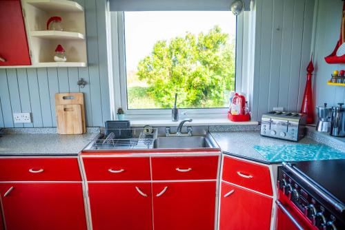 a red kitchen with a sink and a window at Finest Retreats - Western Watch - Sea Views, Pets Accepted, Sleeps 6 in Lower Boscaswell