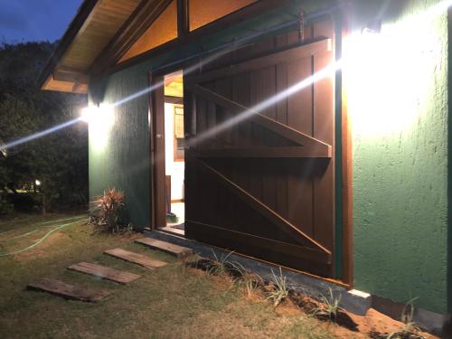a green house with a brown garage door at Pousada Watu Kerere in Praia do Rosa