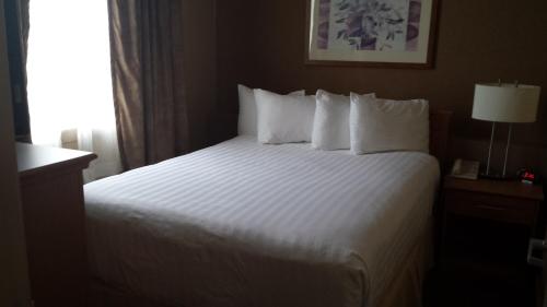 a hotel room with a bed with white sheets and a window at Days Inn & Suites by Wyndham West Edmonton in Edmonton