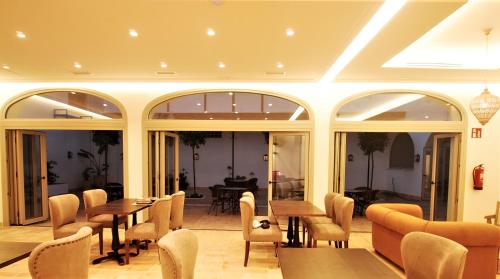 a dining room with tables and chairs and windows at Albariza Hotel Boutique in Sanlúcar de Barrameda