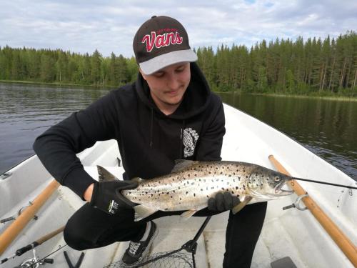 a man in a boat holding a brown trout at Hugsnäset Semesterstugor och Fiske in Gällö