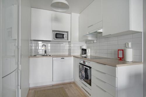 a white kitchen with a sink and a microwave at Kotimaailma Apartments Oulu in Oulu