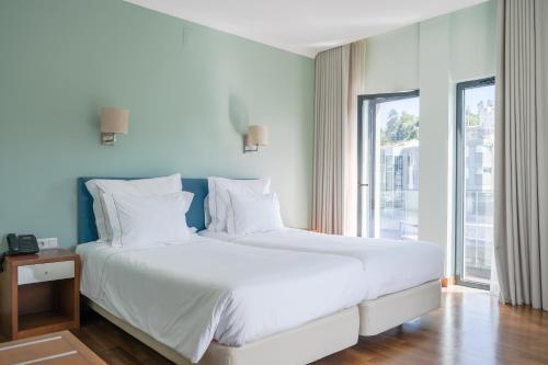 a white bed in a room with a large window at Hotel Vouga in Termas de Sao Pedro do Sul