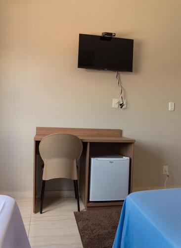 a desk with a chair and a television on a wall at Pouso Oliveira Suítes in São João Batista do Glória