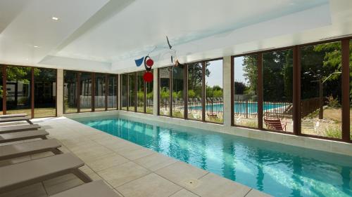 a swimming pool with lounge chairs and a large group of windows at Les Nomades Beaune in Beaune