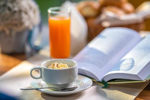 a cup of coffee and a glass of orange juice and an open book at Balneo Hotel Zsori Thermal & Wellness in Mezőkövesd
