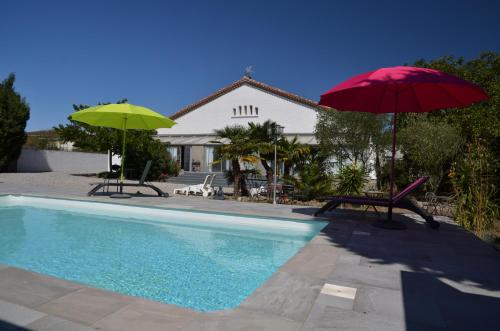 una piscina con due ombrelloni e un tavolo con sedie di Aux Belles Vacances - ADULTS ONLY a Caux-et-Sauzens