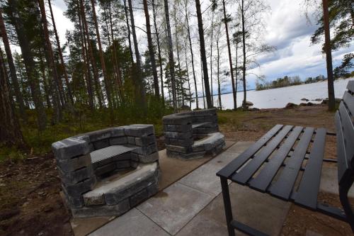 a stone fireplace next to a picnic table and a bench at Pyhtään Vuokramökit in Tuuski