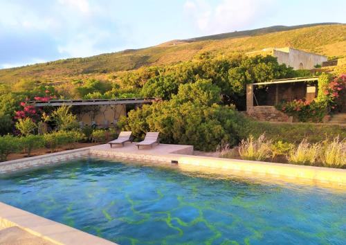 een zwembad in een tuin met twee stoelen en een heuvel bij Tenuta Borgia in Pantelleria
