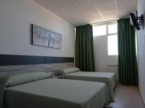 2 camas en una habitación con cortinas verdes en Hostal Brin, en Monreal del Campo
