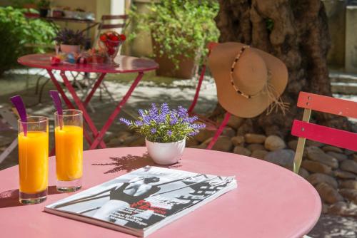 a pink table with two glasses of orange juice and a hat at Hotel du Forum in Carpentras