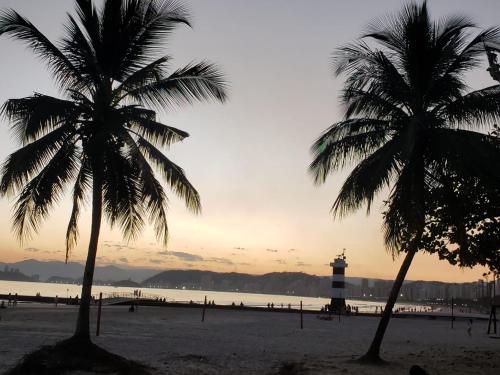 two palm trees on a beach with a lighthouse at Apartamento PÉS NA AREIA in Santos