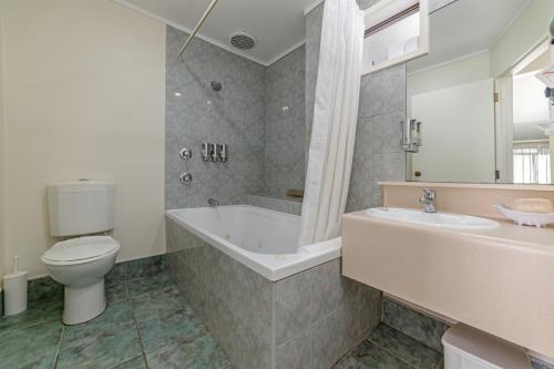 a bathroom with a tub and a toilet and a sink at Legends Motel in Palmerston North