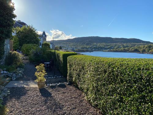 a garden with a hedge and a view of a lake at Fasgadh Rooms in Tarbert