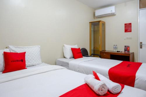 two beds in a room with red and white pillows at RedDoorz near RSUD dr Loekmono Hadi Kudus in Kudus