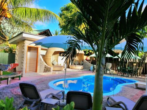 a pool with chairs and an umbrella and a palm tree at Casa De Leela Self Catering Guest House in La Digue