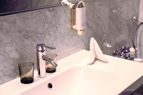 a bathroom sink with a faucet and two glasses on it at Hotel Nolda in St. Moritz