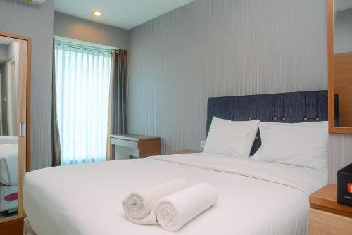 a bedroom with a large white bed with towels on it at Comfortable Studio Grand Kamala Lagoon Apartment By Travelio in Pekayon Satu