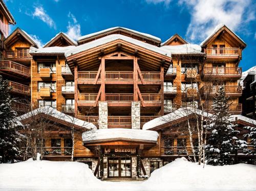 un gran edificio de apartamentos de madera con nieve en el suelo en Hôtel LE BLIZZARD en Val dʼIsère