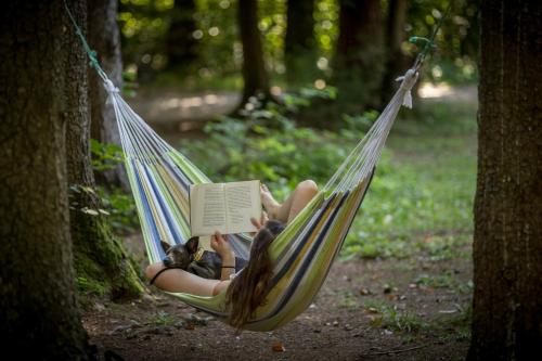 a woman laying in a hammock reading a book at Forest Camping Mozirje in Mozirje