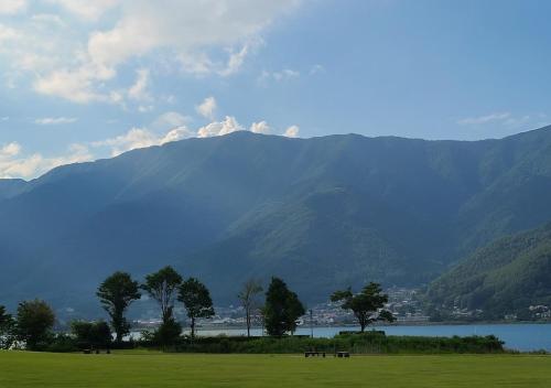 a field with trees and a lake and mountains at Bluebird Hotel in Fujikawaguchiko