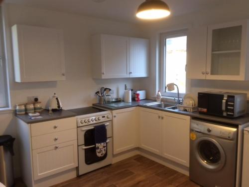 a kitchen with white cabinets and a stove top oven at Centrally located 2 bed modern flat with harbour views in Wick