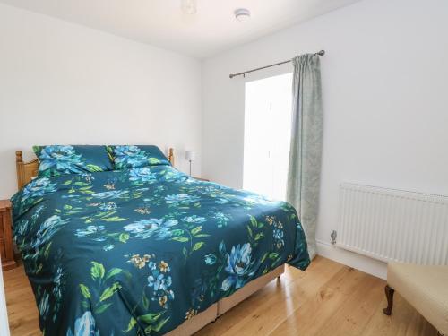 ein Schlafzimmer mit einem Bett mit blauer Decke und einem Fenster in der Unterkunft Waveney View Cottage in Great Yarmouth