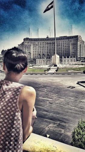 a woman sitting on a ledge looking at a building at Tahrir Square Hostel in Cairo