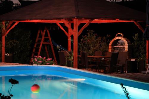 a swimming pool in front of a gazebo at night at Marietta Apartman in Hévíz