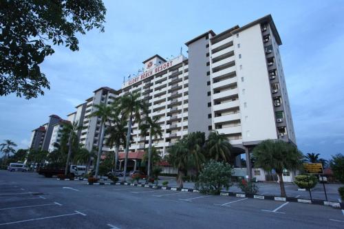 un grande edificio bianco con palme in un parcheggio di GLORY Beach Resort private 2 bedroom apartment a Port Dickson