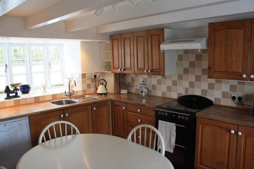 a kitchen with wooden cabinets and a white table at Bojewyan Cottage, Sandy Beaches and Great walking in Penzance