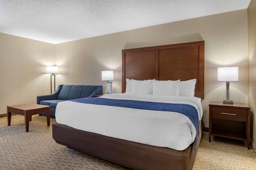 a hotel room with a large bed and a blue chair at Comfort Inn Near Greenfield Village in Dearborn