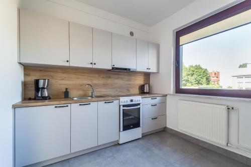 a kitchen with white cabinets and a large window at Apartamenty Robi in Kołobrzeg