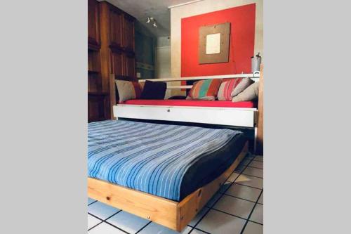 une chambre avec un lit avec un mur rouge dans l'établissement Un pied-à-terre au centre de Papeete, à Papeete