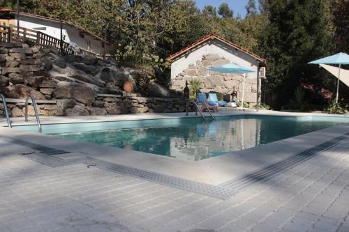 a swimming pool with a stone retaining wall and a house at Bosque dos Amieiros in Marco de Canaveses