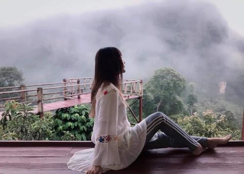 a woman sitting on a deck looking out at a mountain at ม่านฟ้า โฮมสเตย์ MaanFah Homestay in Chiang Rai