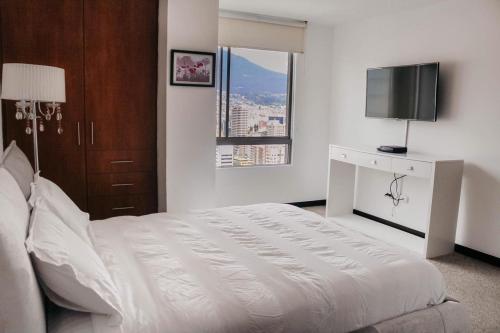 a white bedroom with a bed and a television at Olympus Apartments in Quito