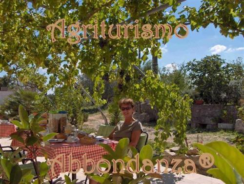 una mujer sentada en una mesa bajo un árbol en Abbondanza® Agriturismo, en Alberobello
