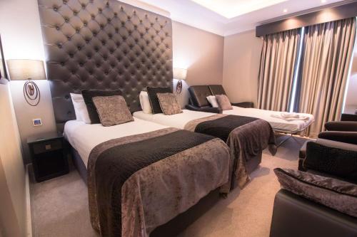 a hotel room with two beds and a couch at The Continental Hotel, Heathrow in Hounslow