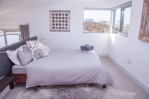 a white bedroom with a bed and a window at Pelicans View in Yzerfontein