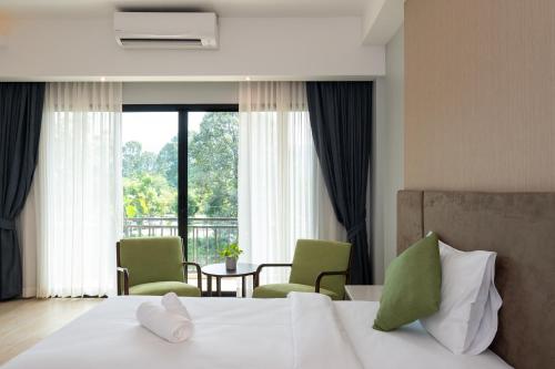 a bedroom with a bed with two chairs and a window at Phumontra Resort Nakhon Nayok in Nakhon Nayok
