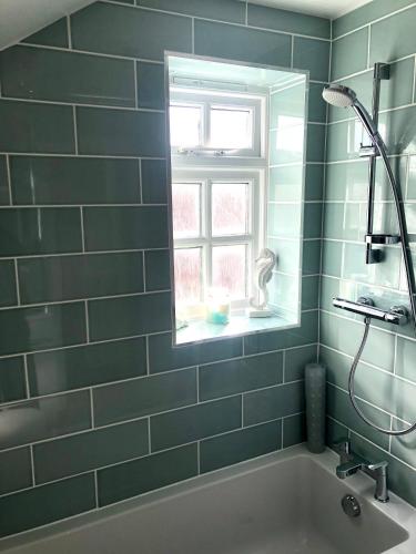 a green tiled bathroom with a tub and a window at Pixie Cottage in Eastbourne