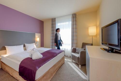 a hotel room with a bed and a woman looking out the window at Mercure Hotel Berlin City West in Berlin