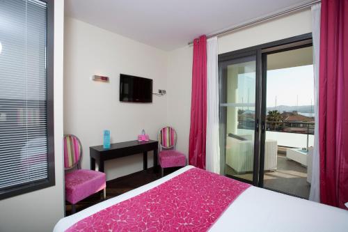 a bedroom with a bed and two pink chairs at Hôtel Baptistin in Le Lavandou