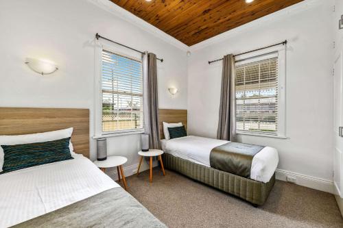 a bedroom with two beds and two windows at Quality Inn Ashby House Tamworth in Tamworth