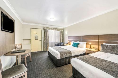 a hotel room with two beds and a desk at Quality Inn Ashby House Tamworth in Tamworth