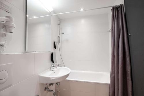 a white bathroom with a sink and a bath tub at Comfort Hotel Lichtenberg in Berlin