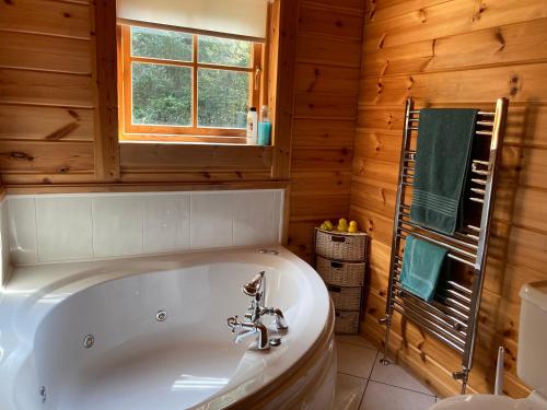 a white tub in a bathroom with a wooden wall at Riverside log cabin in Ballyconnell