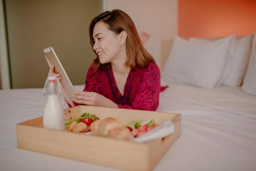 a woman sitting on a bed with a box of food at The Bountie Hotel and Convention Centre Sukabumi in Sukabumi