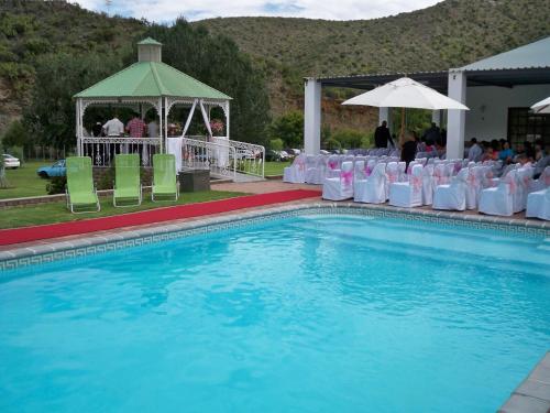 a pool with chairs and a gazebo and a group of people at De Oude Meul Country Lodge & Restaurant in Oudtshoorn